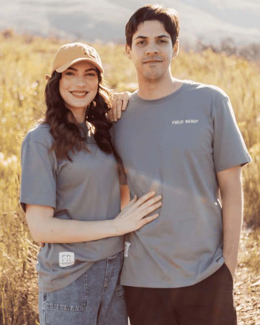 Two people wearing gray t-shirts standing in a field with mountains in the background